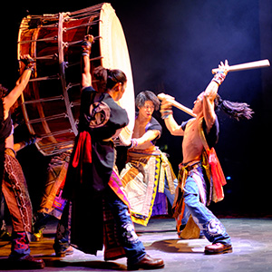 Yamato performers holding a giant drum while another person holds sticks for drumming