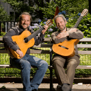 Assad brothers holding guitars and sitting on a bench outdoors